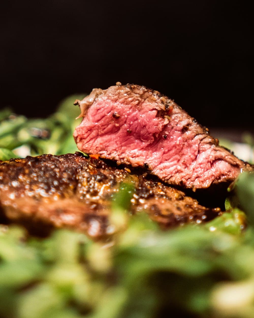 A charcoal-grilled steak, sliced and medium-rare, on a dark plate