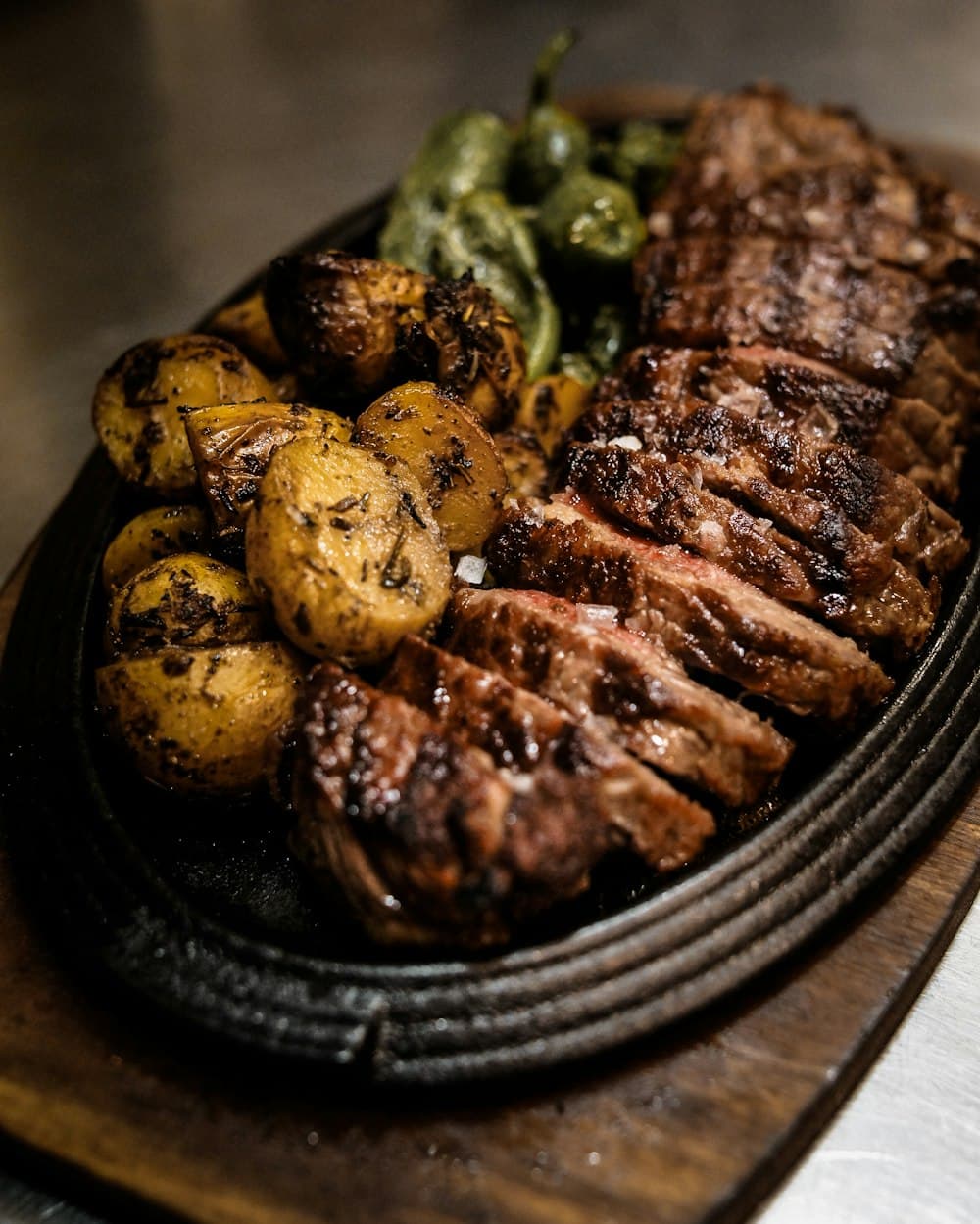 Sliced charcoal-grilled steak with roasted potatoes and peppers